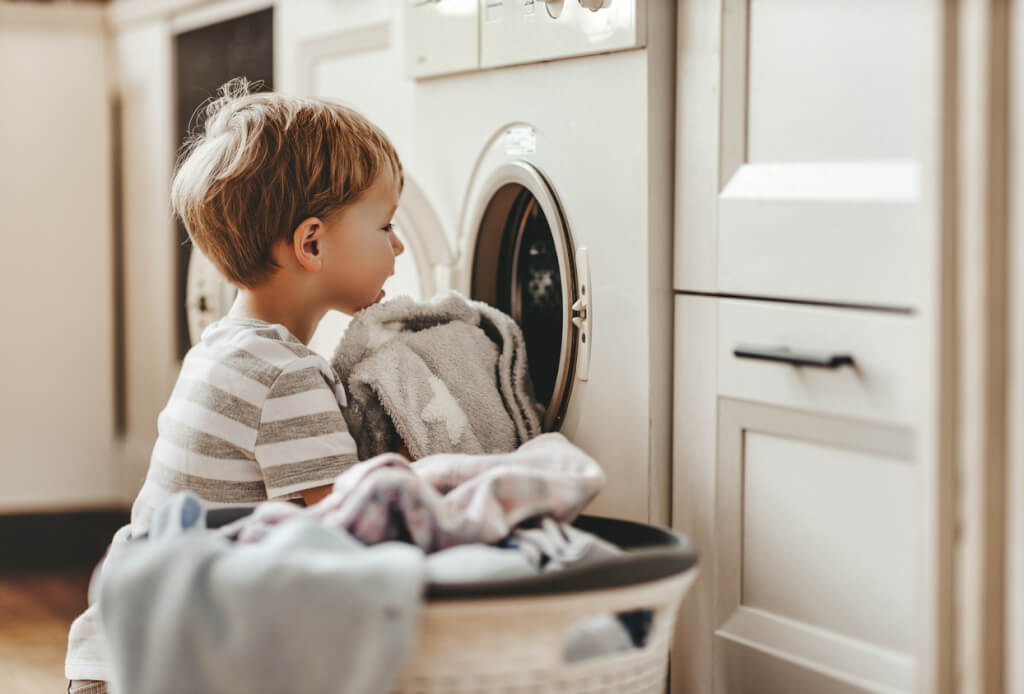 Happy child folding laundry into washing machine