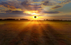 sunrise solar Eclipse with sunbeams through clouds over foggy fields.