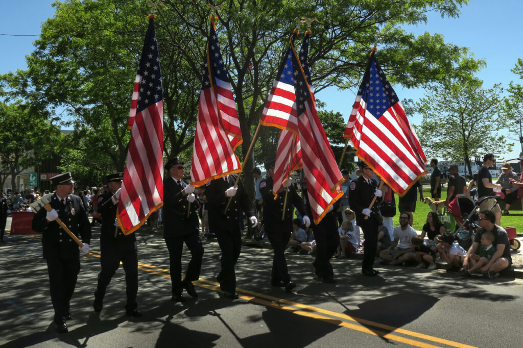 uniformed volunteer firemen marching down Main Street in a small town Memorial Day parade, Greenport, NY