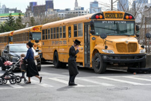 A Jewish Hasidic family crosses a street in Brooklyn. Several yellow school buses in the background.