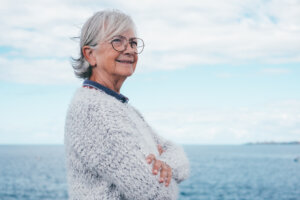 Portrait of pensive handsome senior woman standing by the sea looking away. Smiling elderly white-haired lady in outdoor excursion enjoying freedom, relax and retirement