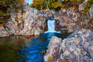 Image of Tiers of waterfalls pouring over rocks into calm river from below in forest