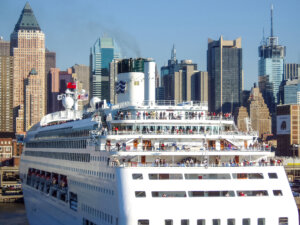A cruise ship setting sail with passengers from the Hells Kitchen Pier with the Midtown Manhattan cityscape in the background in New York City, USA.