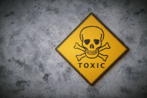 A square yelow sign with the international symbol for poison and other chemical / biological hazard. The sign is set on a dirty concrete wall surface.