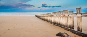 A wooden fence on an empty beach at sunset