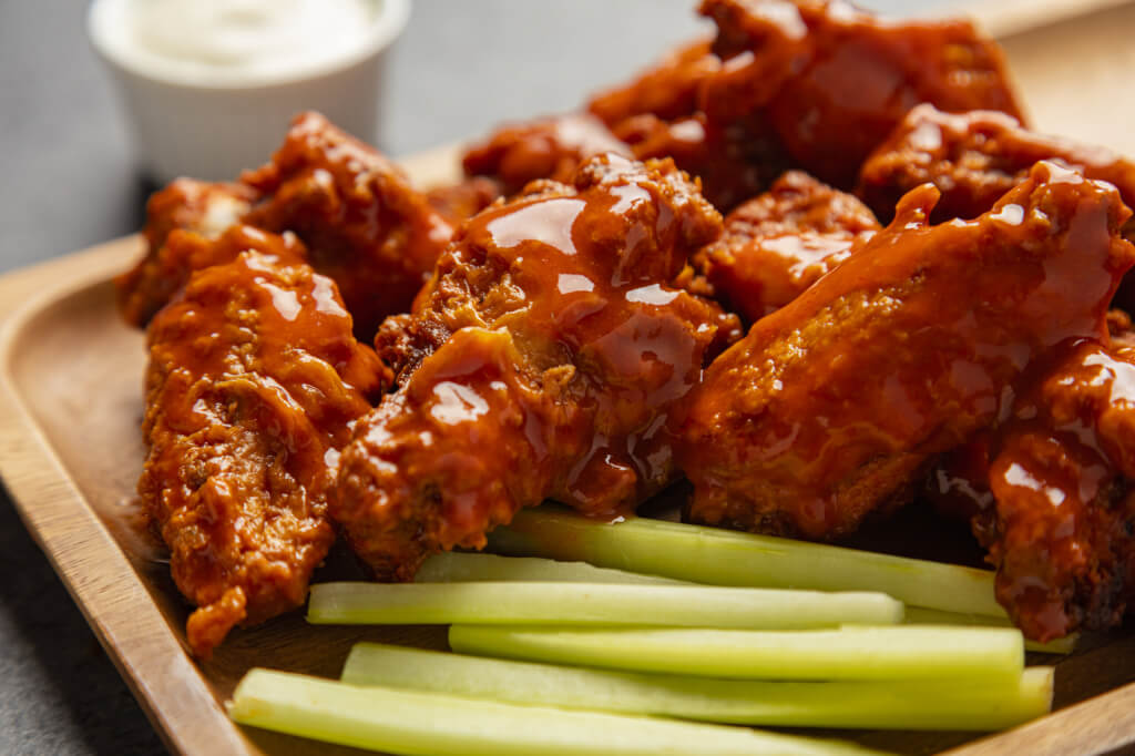 Traditional Buffalo style chicken wings on a wooden plate with celery and ranch dressing
